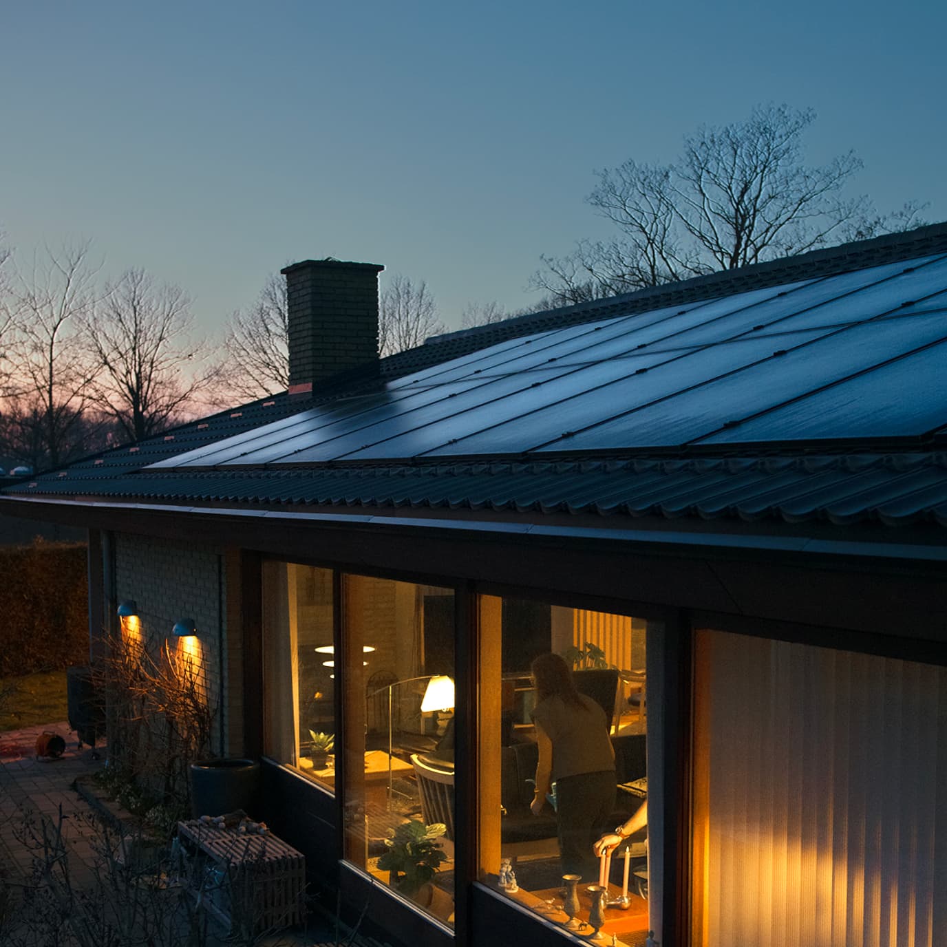 Solceller på tag om aftenen med lys i vinduerne