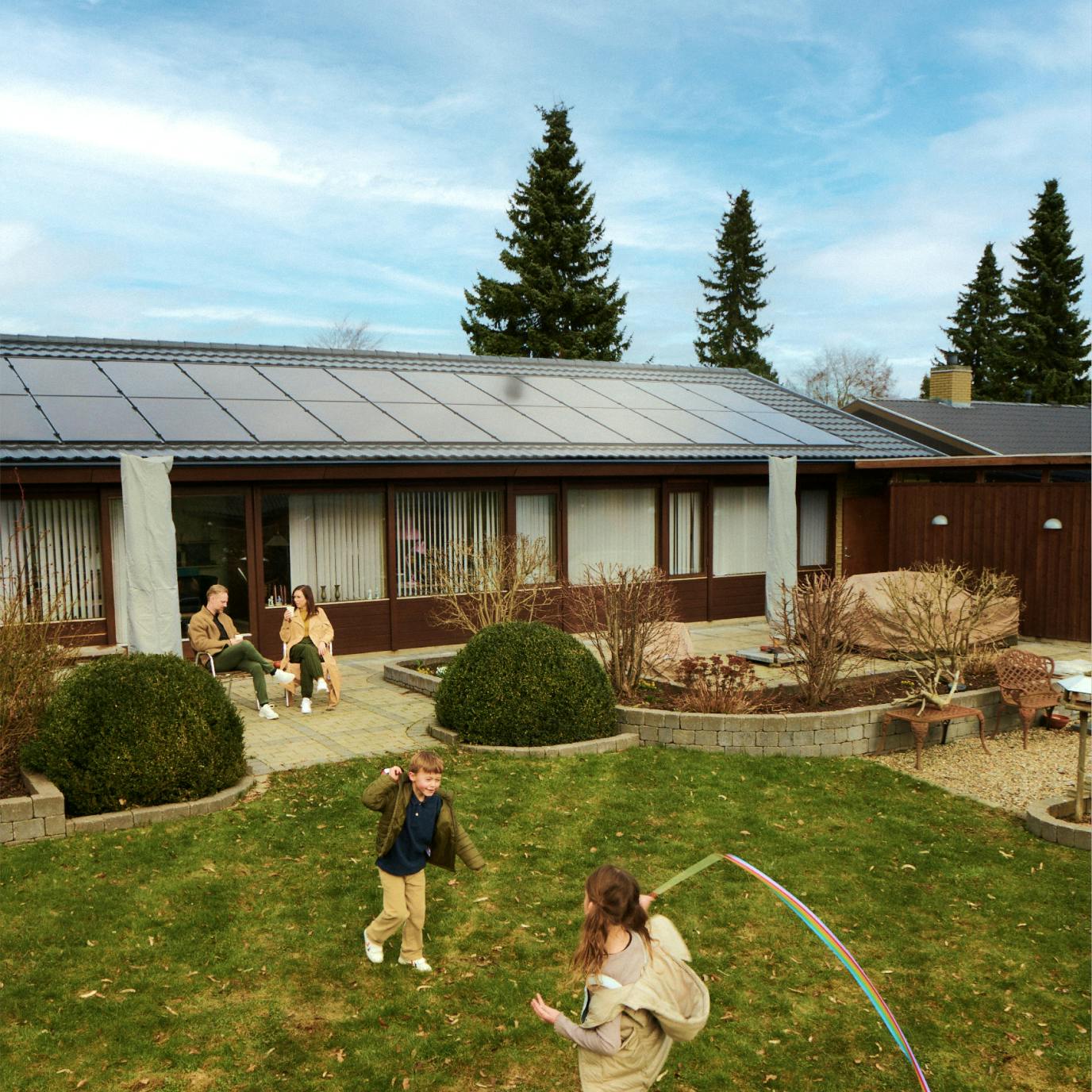 Familie i haven med solceller på taget i baggrunden